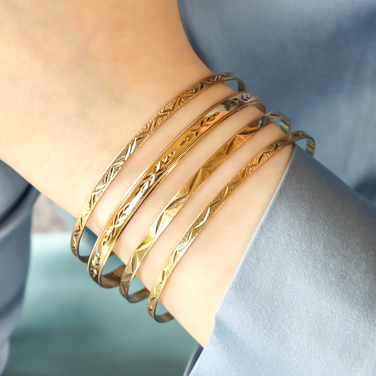 Model wears 9ct Yellow Gold 3mm Diamond Cut Feather Stacking Bangle, 9ct Yellow Gold 5mm Diamond Cut Leaf Stacking Bangle, 9ct Yellow Gold 3mm Diamond Cut Leaf Stacking Bangle & 9ct Yellow Gold 3mm Diamond Cut Fine Leaf Stacking Bangle