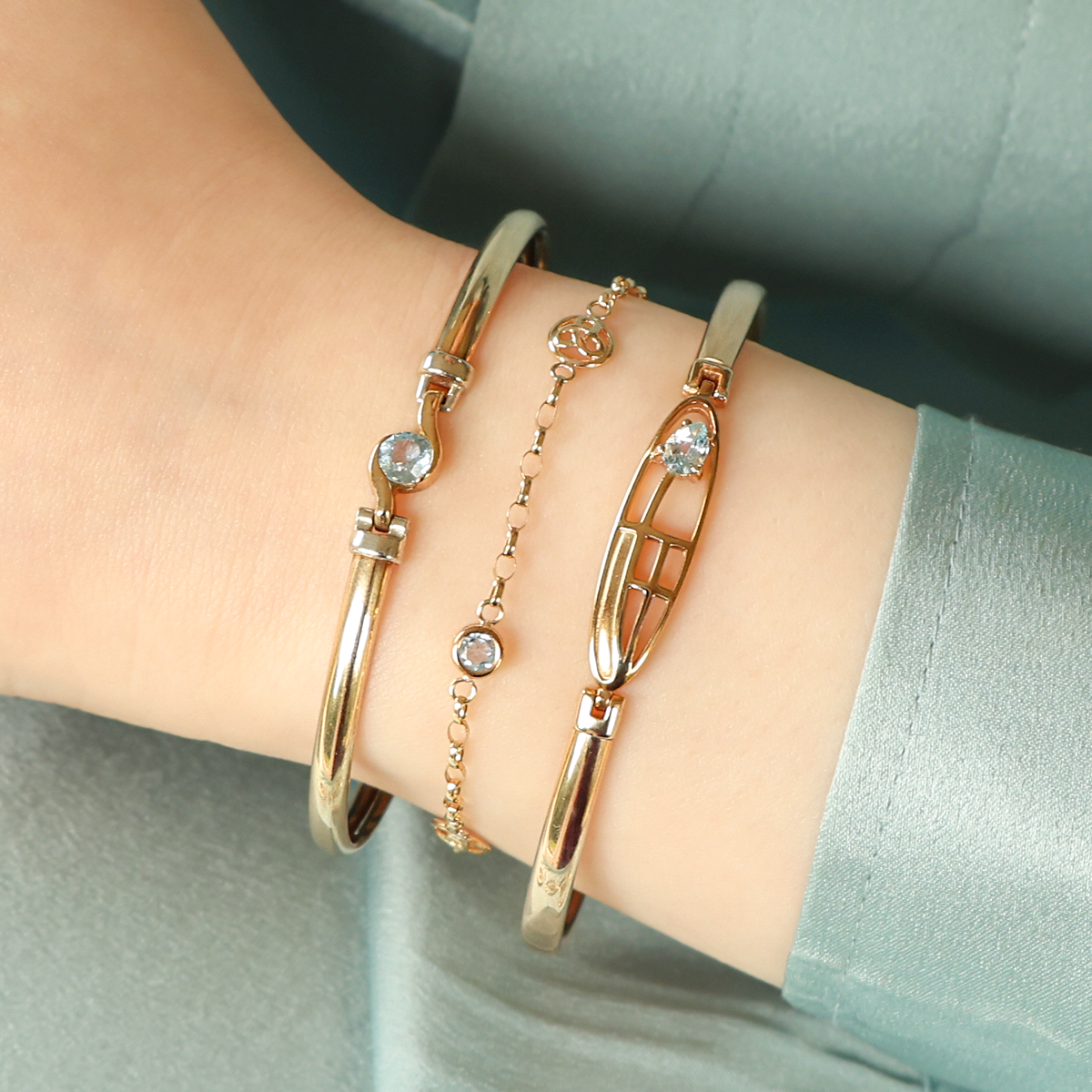 Model wears 9ct Yellow Gold Blue Topaz Tension Bangle, 9ct Yellow Gold Trinity Knot Blue Topaz Bracelet & 9ct Yellow Gold Blue Topaz Rennie Mac Tension Bangle