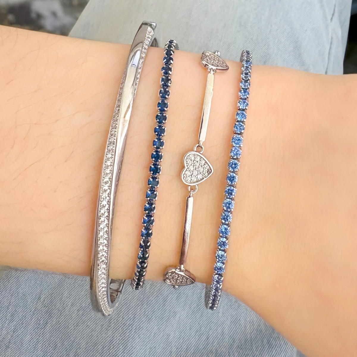 Model wears Sterling Silver Cubic Zirconia Twisted Hinged Bangle, Sterling Silver Dark Blue Cubic Zirconia Tennis Bracelet, Sterling Silver Cubic Zirconia Station Bracelet & Sterling Silver Light Blue Cubic Zirconia Tennis Bracelet