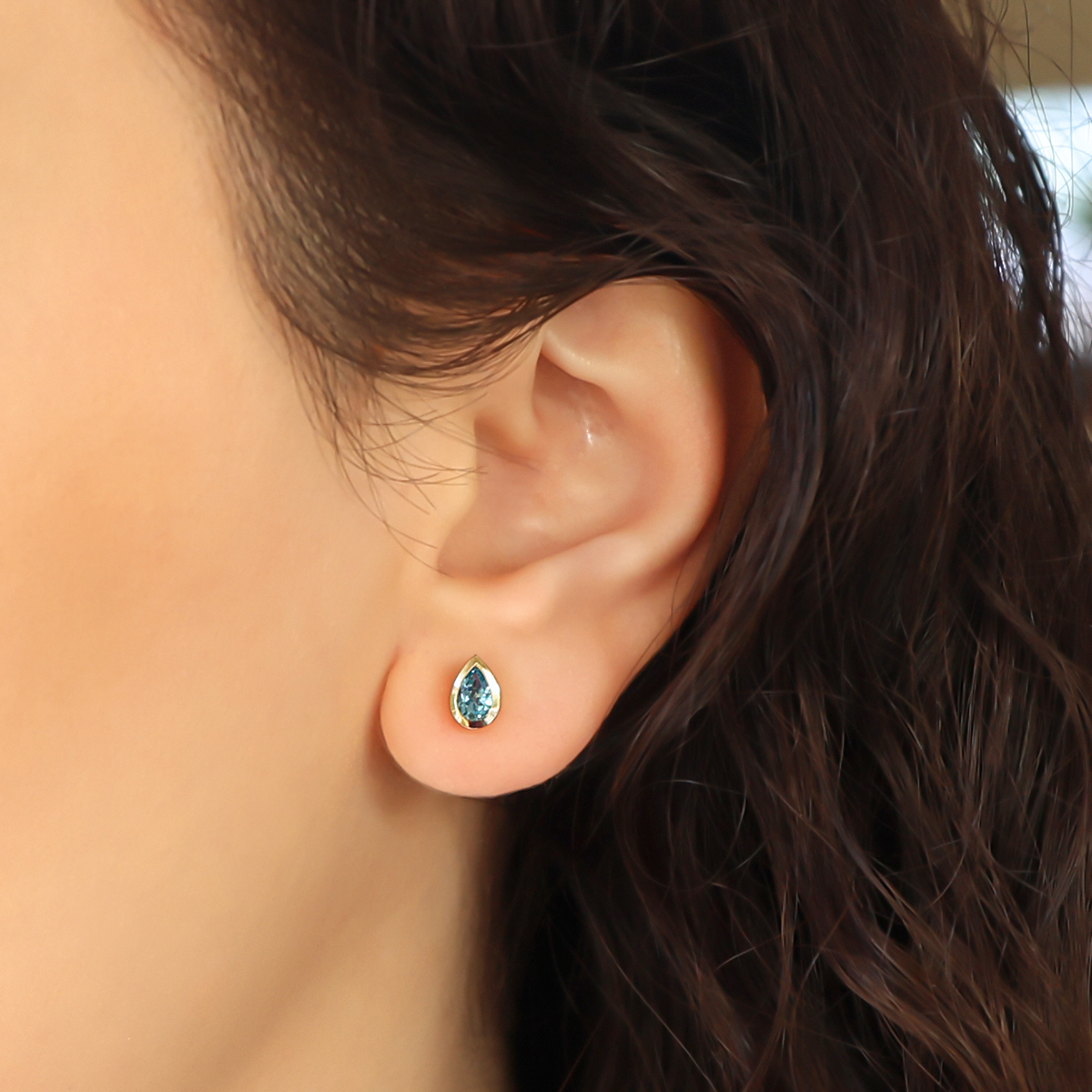Model wears 9ct Yellow Gold Pear Shaped Blue Topaz Bezel Set Stud Earrings