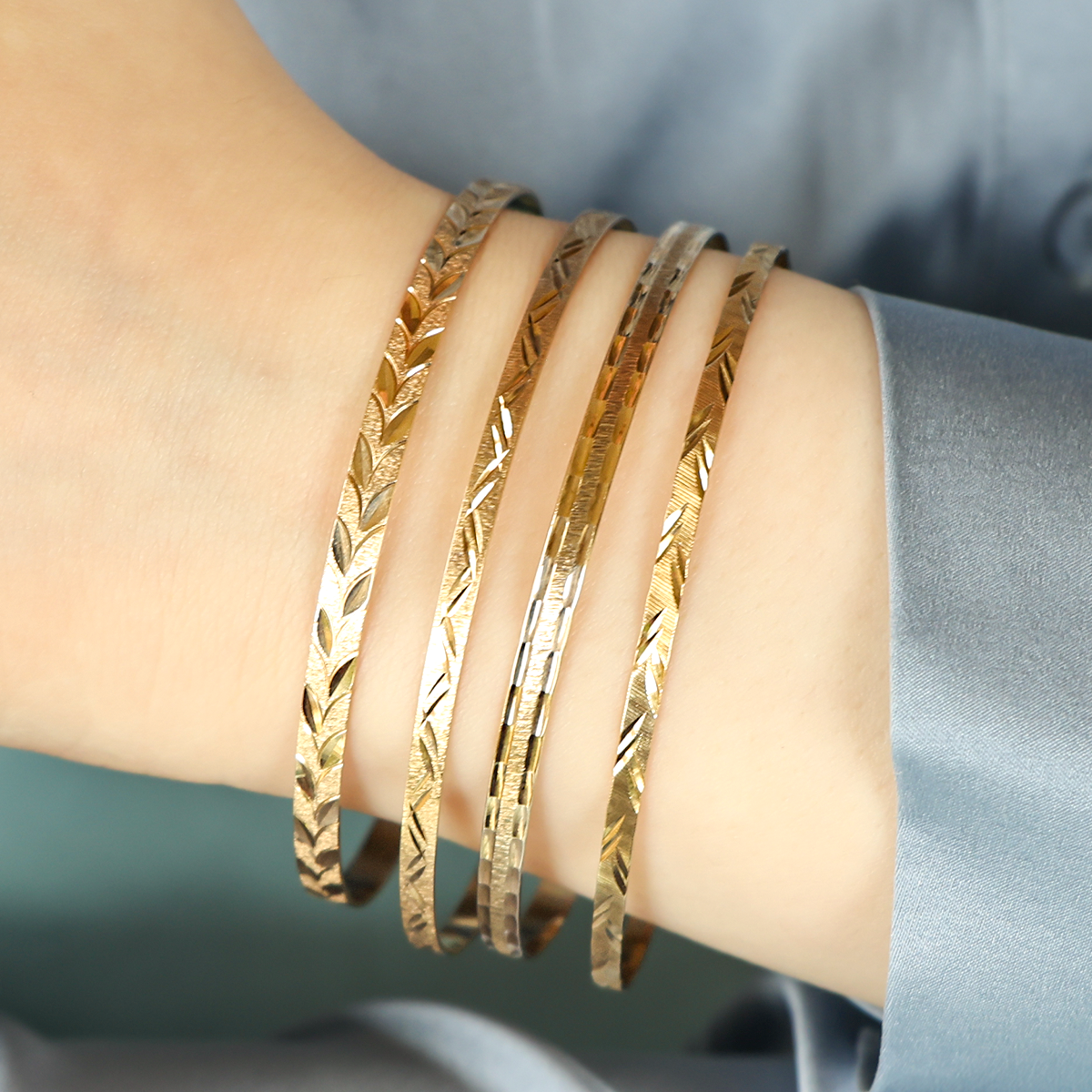 Model wears 9ct Yellow Gold 4mm Leaf Diamond Cut Stacking Bangle, 9ct Yellow Gold 3mm Diamond Cut Double Feather Stacking Bangle, 9ct Yellow Gold 4mm Textured Diamond Cut Stacking Bangle & 9ct Yellow Gold 3mm Diamond Cut Double Leaf Stacking Bangle