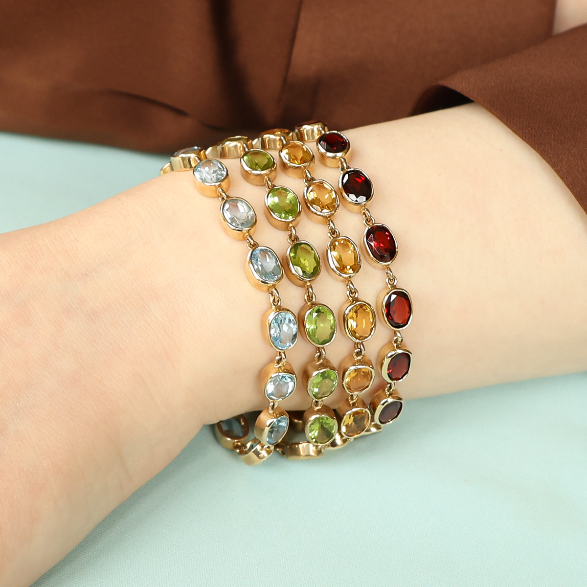 Model wears a stack of 9ct Yellow Gold Blue Topaz, Peridot, Citrine & Garnet Bezel Set Bracelets