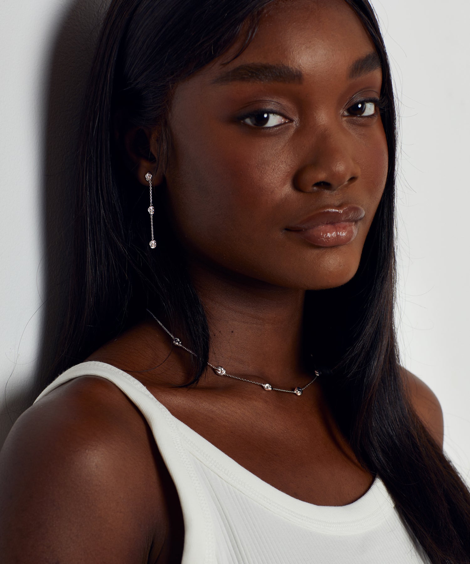 Female model wearing matching silver station knot drop earrings and necklace.