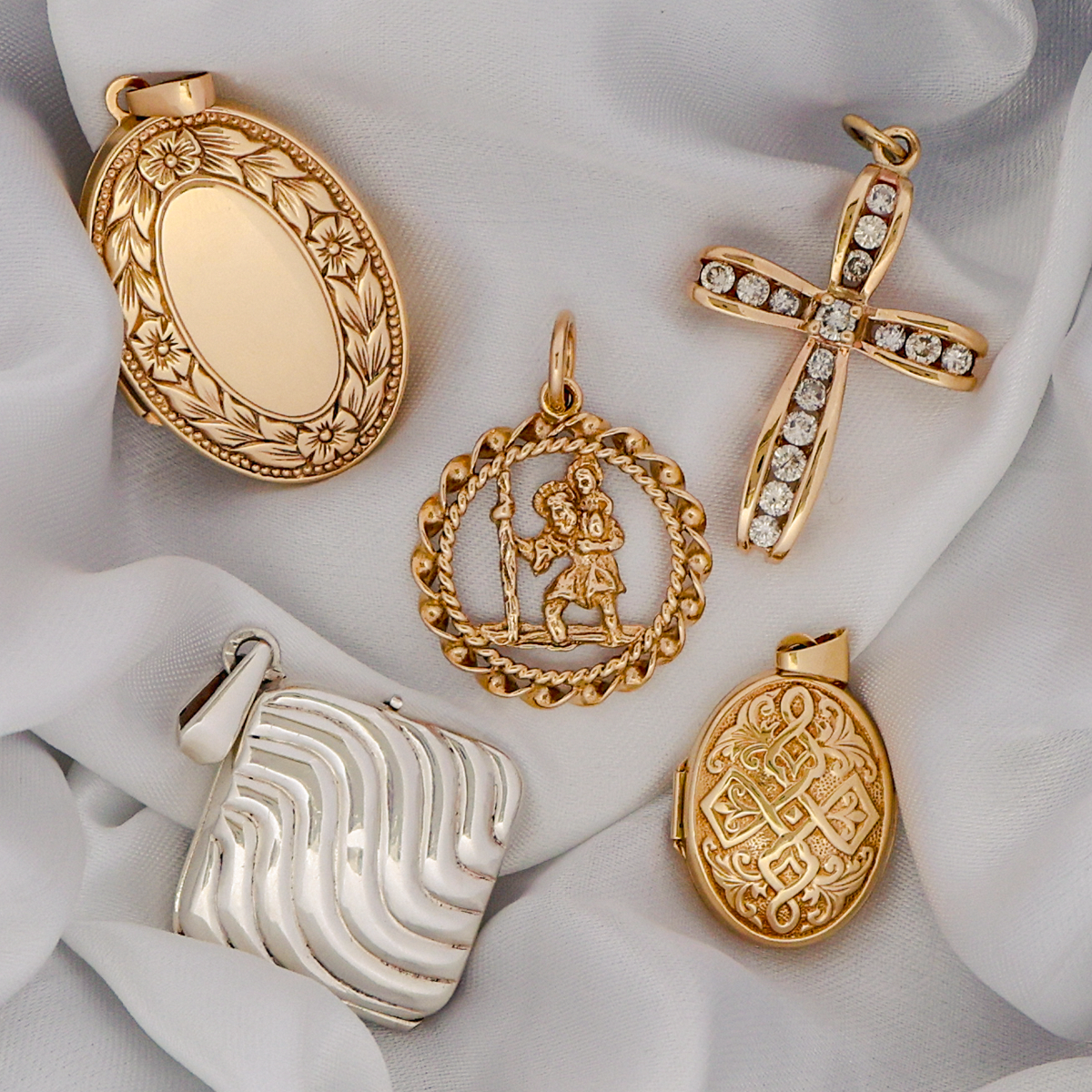 Collection of gold and silver jewellery pendants including a St Christopher, diamond set cross, oval shaped lockets and rhombus shaped locket on a white fabric background.