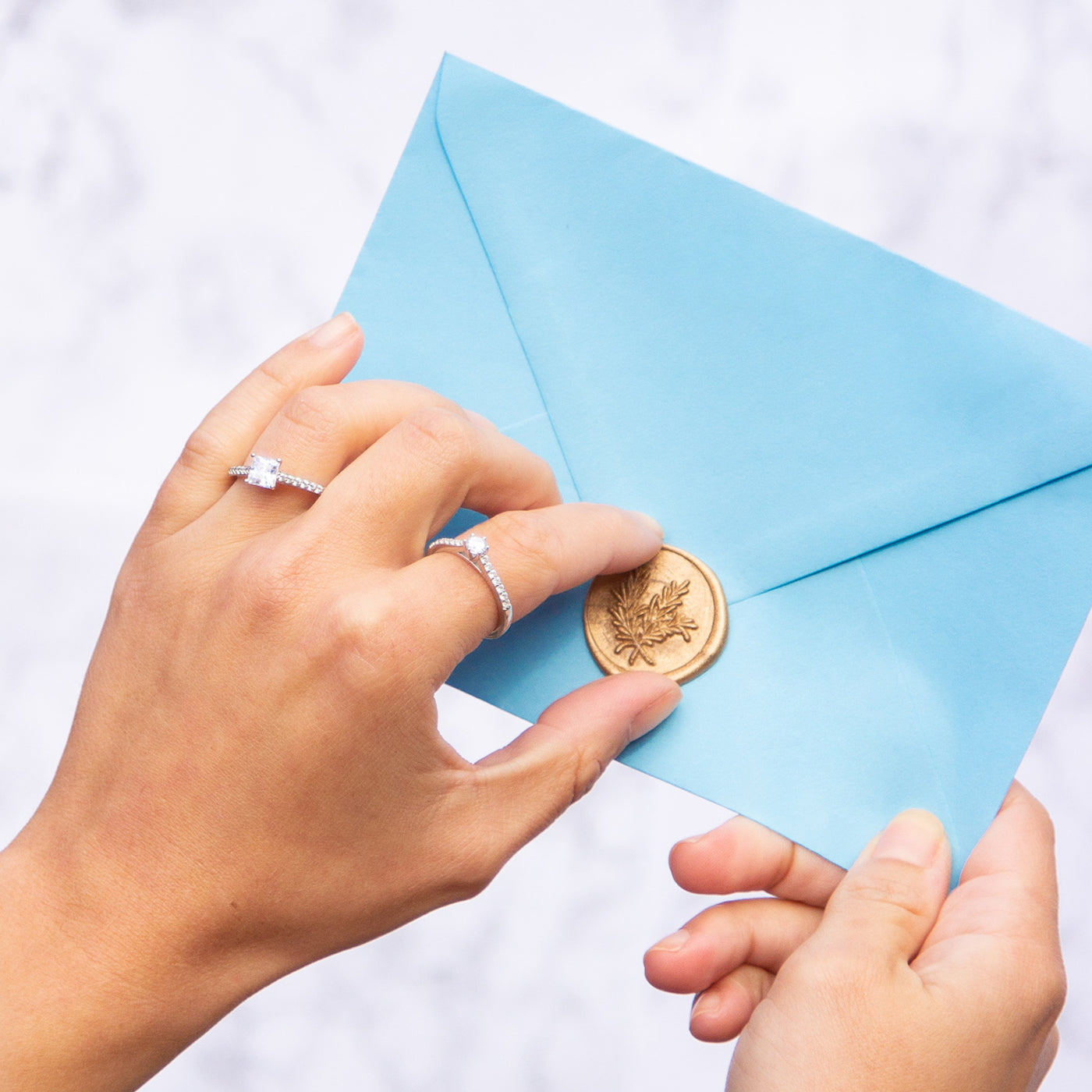 Model wearing diamond solitaire with shoulders engagement rings and holding a sealed enevelope.